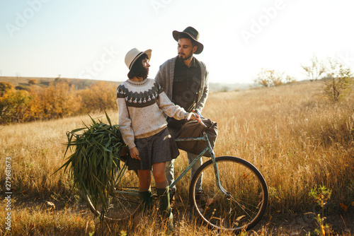 Lovely hipster couple with bike . Couple wearing beautiful hats and sweaters. Lifestyle, happy couple of two play on a sunny day in the park. The concept of youth, love and lifestyle. Sunset in autumn