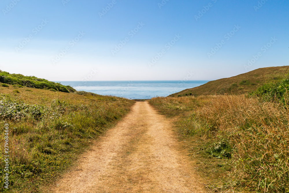 Looking down a pathway towards the sea with a blue sky overhead, at the Sussex coast