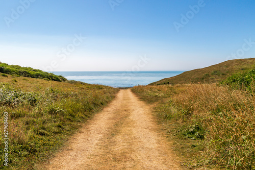 Looking down a pathway towards the sea with a blue sky overhead, at the Sussex coast