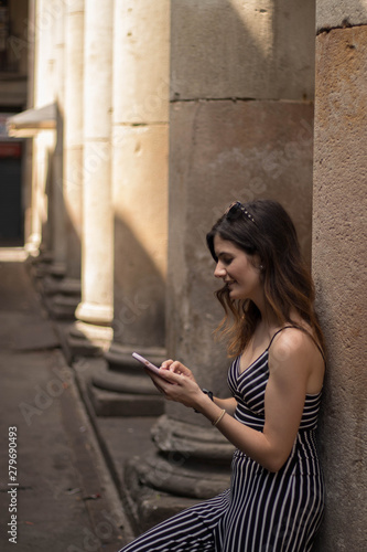 Mujer joven hermosa sonríe mientras envía mensajes en la calle