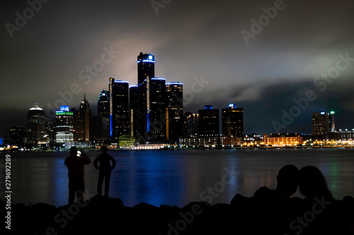 Silhouette of a man taking photo of his kid with Detroit skyline at the background