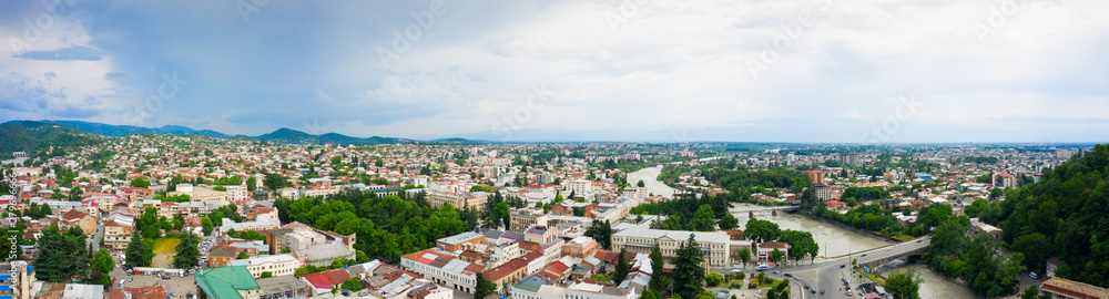 Panoramic summer view of the city of Kutaisi, Georgia. Blue sky with clouds. River Rioni and old houses with Red roofs. Mountains in the distance.