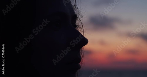 Close up side view of female face silhouetted by sunset evening light on colorful sky background. Macro portrait of young woman looking aside outdoors copy space. Emotion problem depression concept