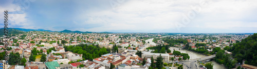 Panoramic summer view of the city of Kutaisi, Georgia. Blue sky with clouds. River Rioni and old houses with Red roofs. Mountains in the distance. © miklyxa