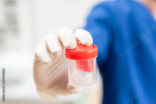Drug test. Doctor in blue uniform and medical gloves holding a container for semen analysis. Donor sperm for artificial insemination, infertility treatment, planning of children