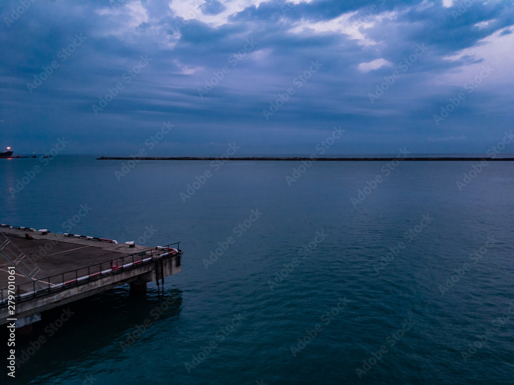 Sea pier in the summer morning surrounded by green sea water and with dark clouds on the horizon.