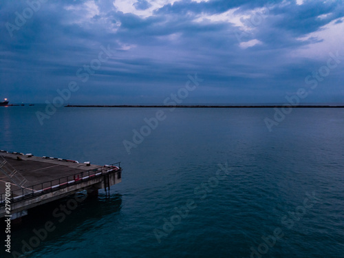 Sea pier in the summer morning surrounded by green sea water and with dark clouds on the horizon.