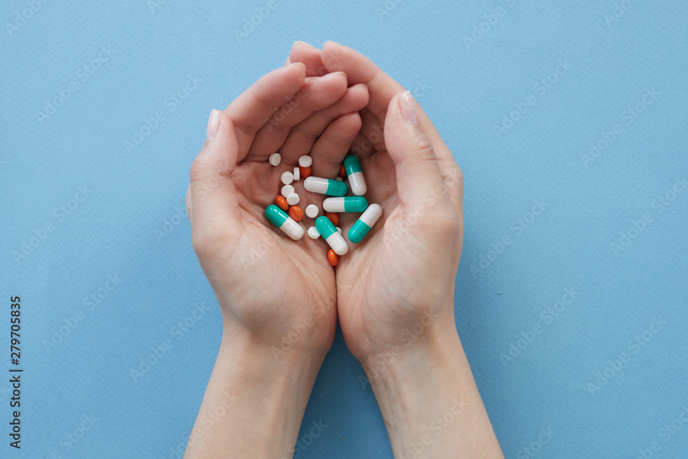 High angle view of unrecognizable woman with handful of pills against blue background