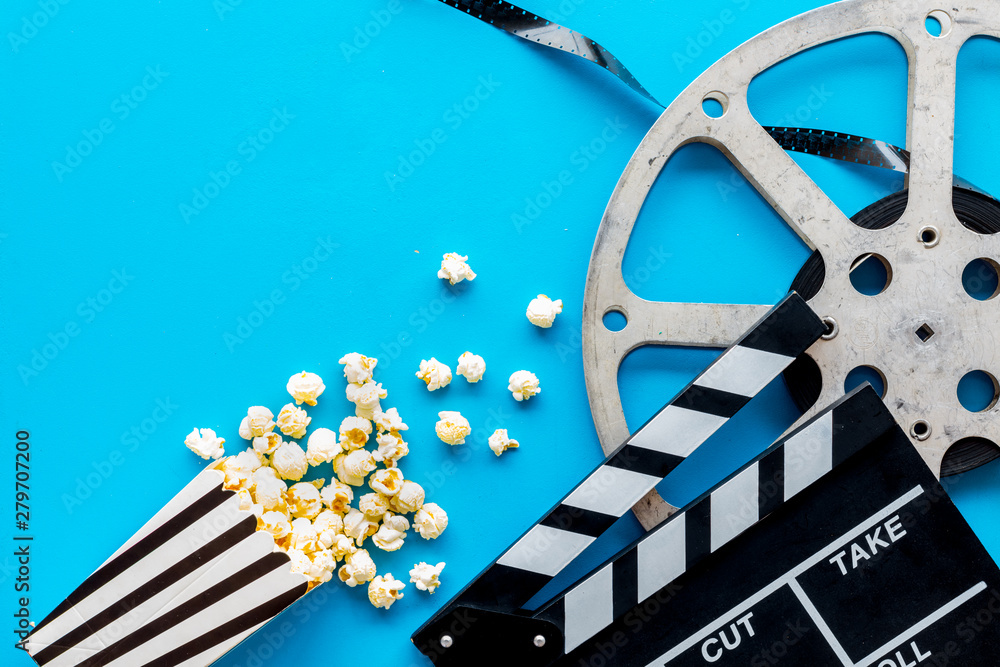 Watch film in cinema with popcorn, video tape and clapperboard on blue background top view