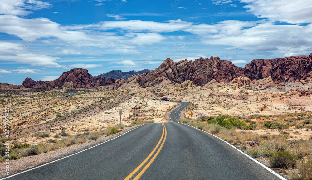 Long winding highway with ups and downs, cloudy blue sky. Valley of Fire Nevada, USA