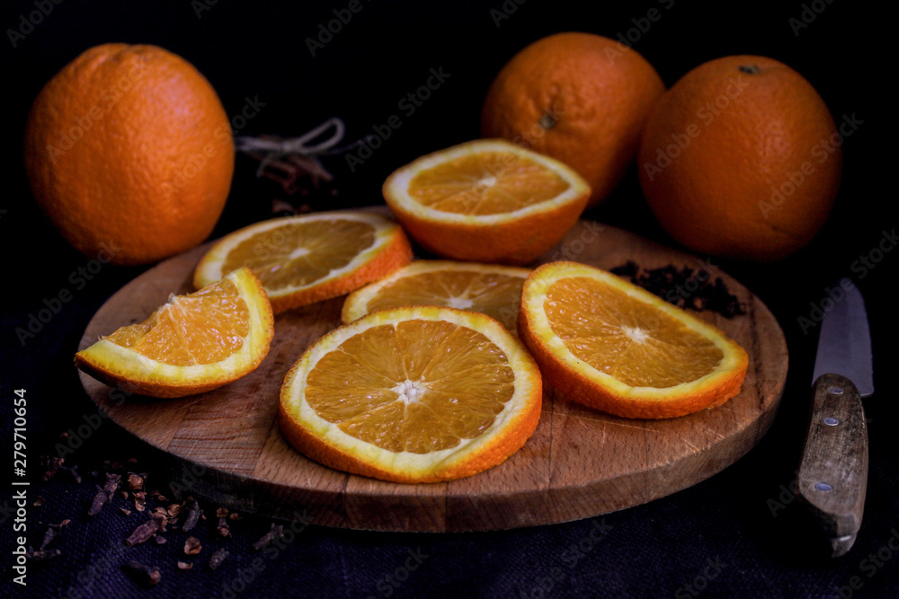 Halves and whole oranges on wooden board over black background, close up Halves and whole oranges on wooden board over black background, close up