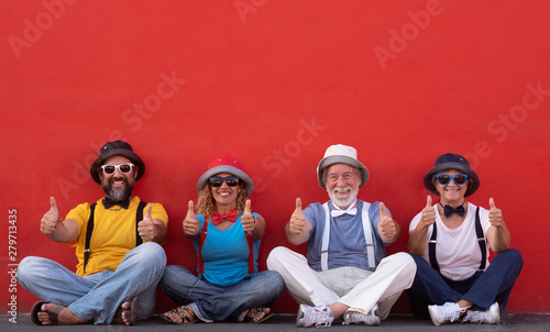 Canvas-taulu Smiling group of four people sitting against a red wall enjoying friendship gesturing ok with hands