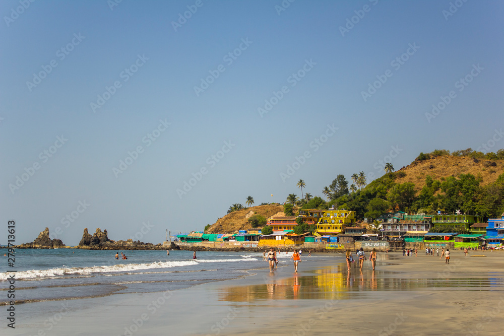 Arambol, Goa/India - 04.01.2019: people walk along the sandy beach of the coast and swim in the ocean near the bright hotels near the hill with palm trees
