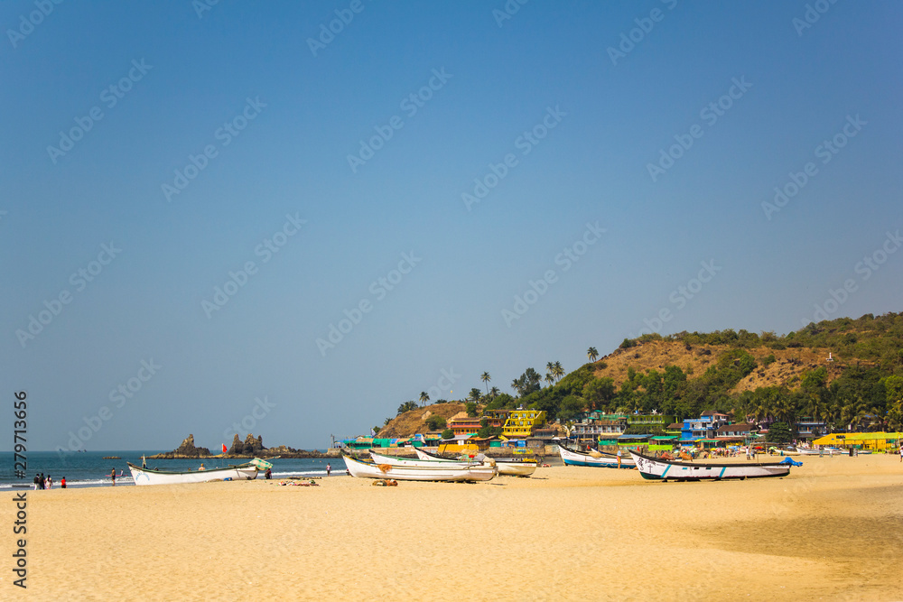 Arambol, Goa/India - 04.01.2019: sandy beach on the sea coast with boats in the background of bright houses and a hill with palm trees