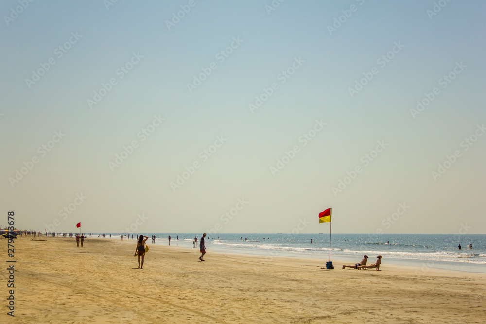 Arambol, Goa/India - 04.01.2019: sandy coast of the ocean coast with walking and bathing people and a lifeguard flag
