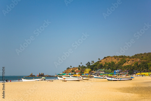 Arambol, Goa/India - 04.01.2019: sandy beach on the sea coast with boats in the background of bright houses and a hill with palm trees