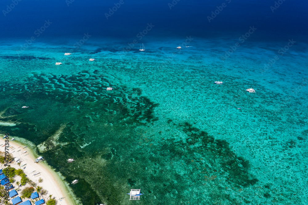 Aerial view of traditional Bangka boats moored above a large tropical coral reef in a calm ocean (Malapascua, Philippines)