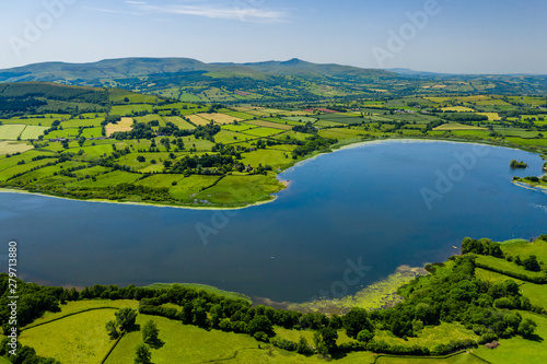 Fototapeta Naklejka Na Ścianę i Meble -  Aerial view of a lake surrounded by green, rolling farmland (Llangorse Lake, Wales)