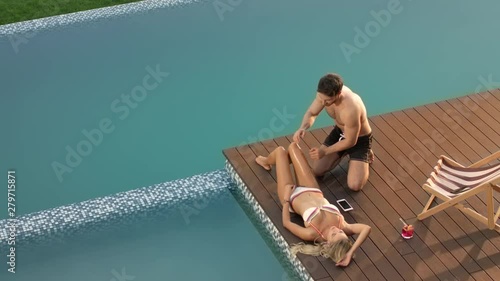 Sexy man applying suntan lotion on female body. Happy couple enjoying sunbathing