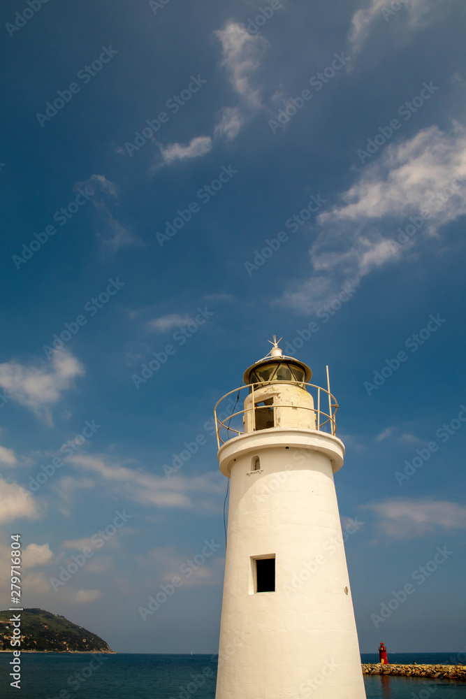 Low angle vertical view of a white lighthouse with a cape in the background against blue sky and sea in a sunny summer day, Porto Maurizio, Imperia, Liguria, Italy