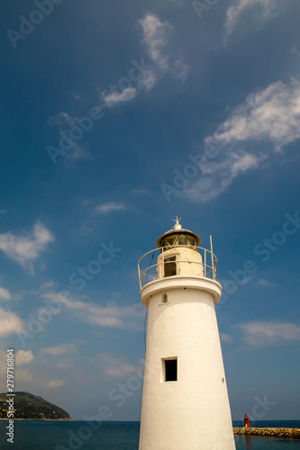 Low angle vertical view of a white lighthouse with a cape in the background against blue sky and sea in a sunny summer day, Porto Maurizio, Imperia, Liguria, Italy