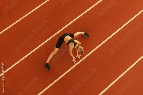 sportswoman doing stretching exercise before run on racetrack stadium, top view, overall plan