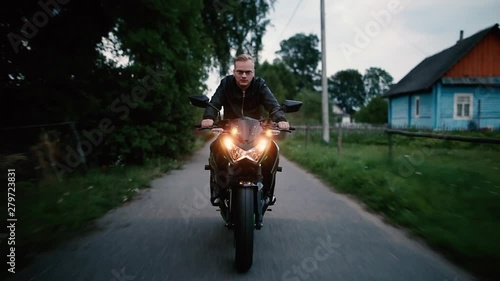 young male biker rides a modern motorcycle along an empty road in the evening. Biker life style.