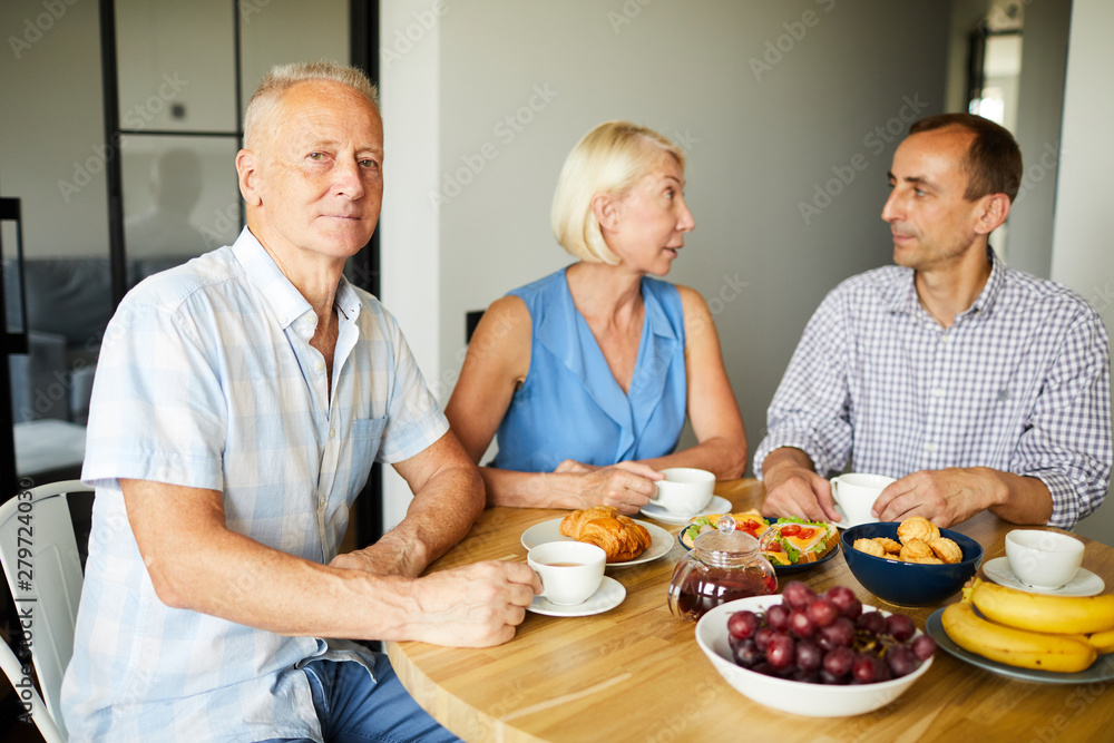 Portrait of senior man sitting at dinner table and smiling at camera while enjoying lunch with friends and family, copy space Portrait of senior man sitting at dinner table and smiling at camera while enjoying lunch with friends and family, copy space