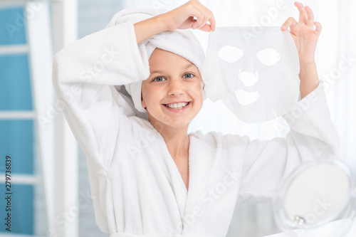 Smiling little girl make face skin mask with towel on head