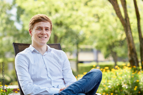Young attractive man in white shirt sitting on brown chair in the park on green background