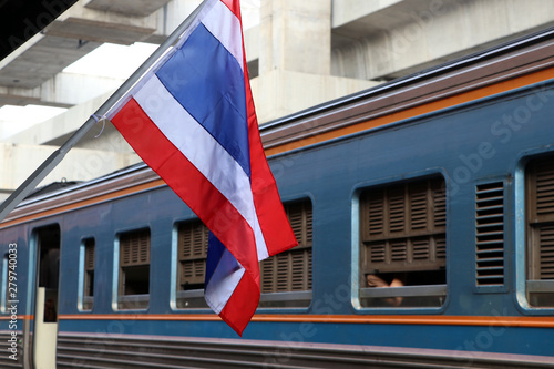 Thai flag at train station and background the train is leaving the station.