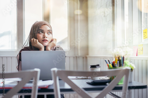 Attractive asian muslim business woman brown hijab working at home looking outside. photo