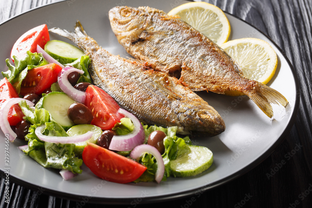 Spicy fried Salema porgy sea fish with lemon and fresh vegetable salad close-up on a plate. horizontal Spicy fried Salema porgy sea fish with lemon and fresh vegetable salad close-up on a plate. horizontal