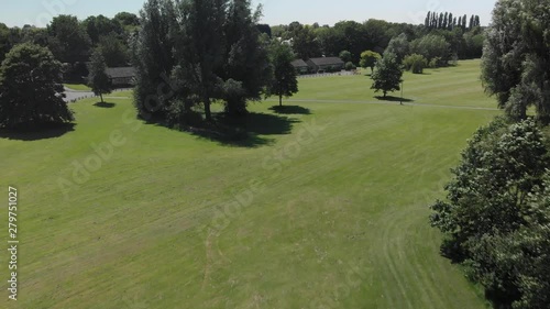 Pulling back over a field and trees in an urban green space on a Summer day in Manchester, England.