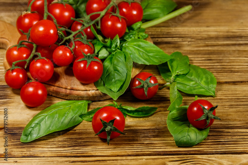 Fresh cherry tomatoes with green basil leaves on a wooden table