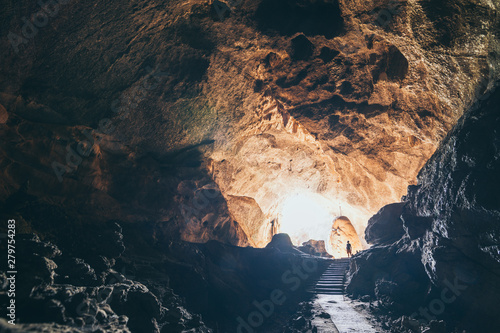 Human silhouette stands inside the cave with light coming from the ceiling