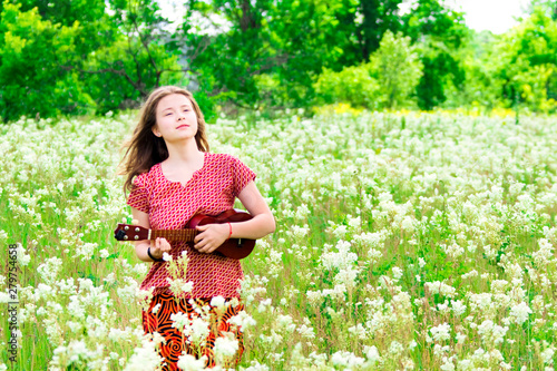 Inspired girl with ukulele among flowers in the meadow.