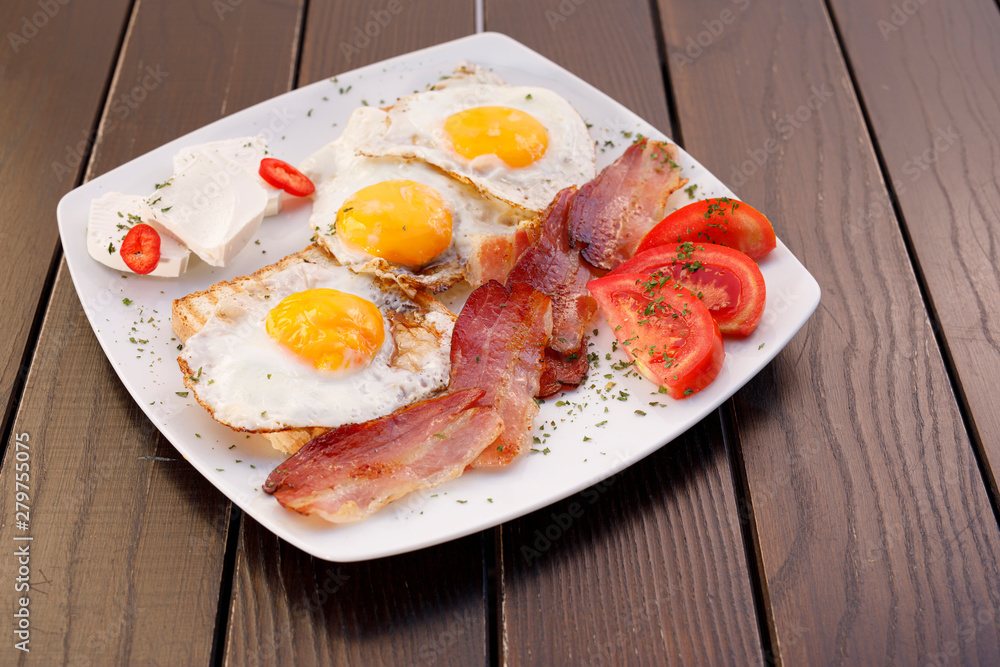 Healthy bacon fried egg on toast bread breakfast on plate , fresh tomatoes and cheese on plate , wood background. Healthy bacon fried egg on toast bread breakfast on plate , fresh tomatoes and cheese on plate , wood background.