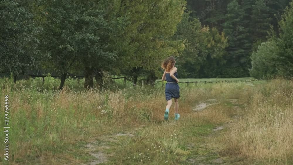 Running young girl teenager in dress on country road, nature background rustic style, back view Running young girl teenager in dress on country road, nature background rustic style, back view