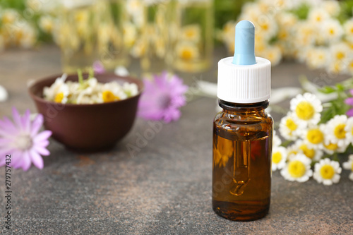 Bottle of essential oil with wild flowers on grey table