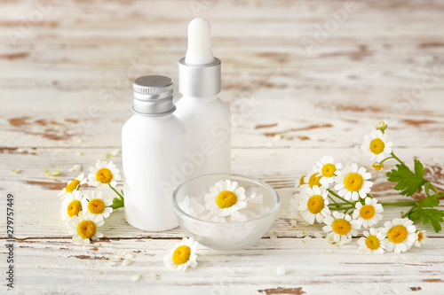 Bottles of cosmetic product with chamomile flowers on white table