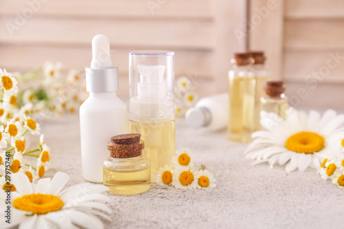 Bottles of cosmetic products with chamomile flowers on table
