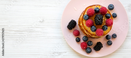 Pancakes with berries and honey on a pink plate, top view. Overhead, flat lay, from above. Copy space.