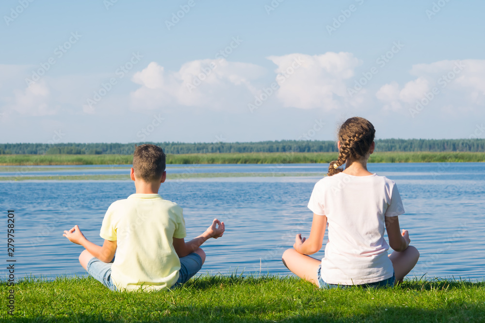 boy and girl sit on the green grass and do yoga, rear view, against the backdrop of a beautiful landscape boy and girl sit on the green grass and do yoga, rear view, against the backdrop of a beautiful landscape