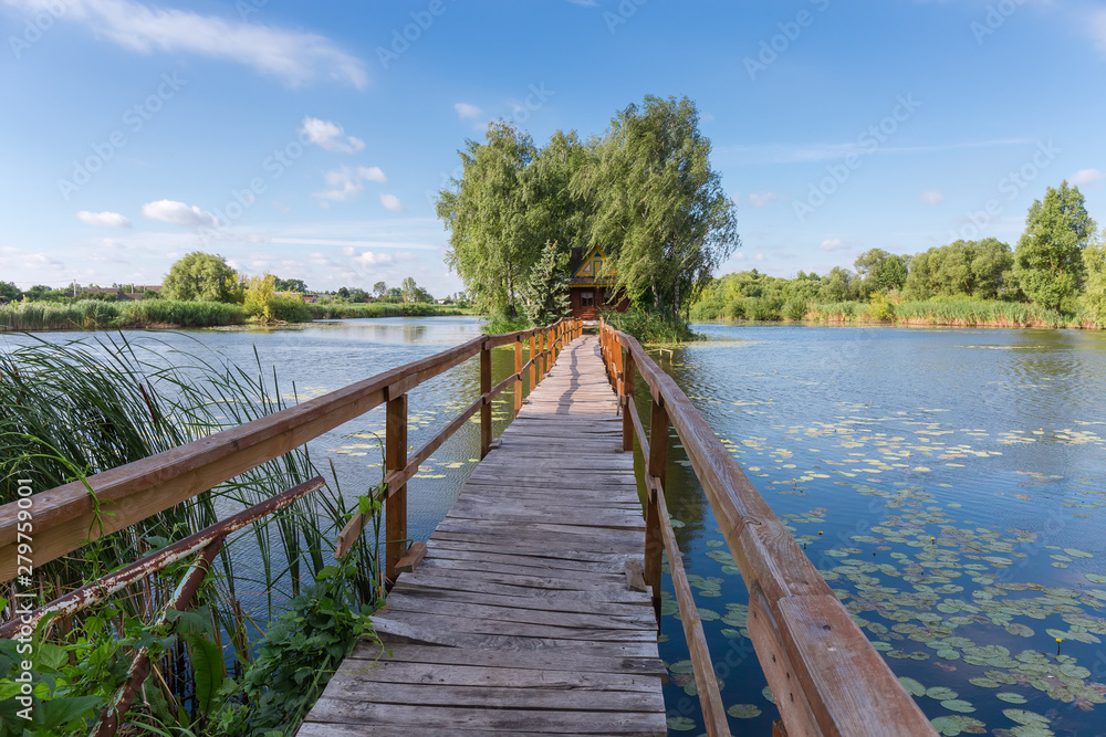 Wooden footbridge to island with hut and trees on lake