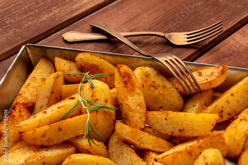 Potato wedges, oven roasted with rosemary, in a baking tray on a dark rustic wooden background photo