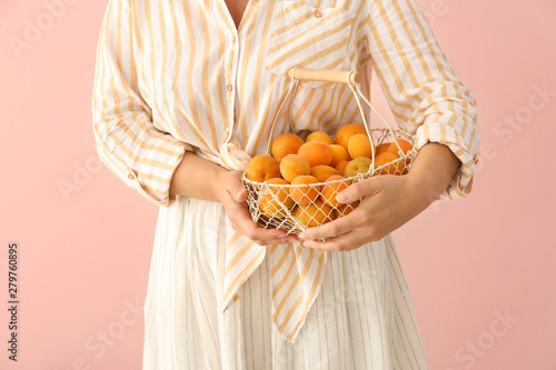 Woman with basket full of ripe apricots on color background