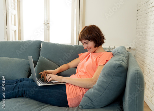 Happy young woman working on her laptop sitting on the sofa. In education and working concept