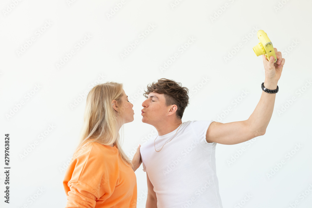 Funny young couple in love cute man and charming woman making selfie on vintage yellow film camera posing on a white background. Concept lovers of photography and hobbies.