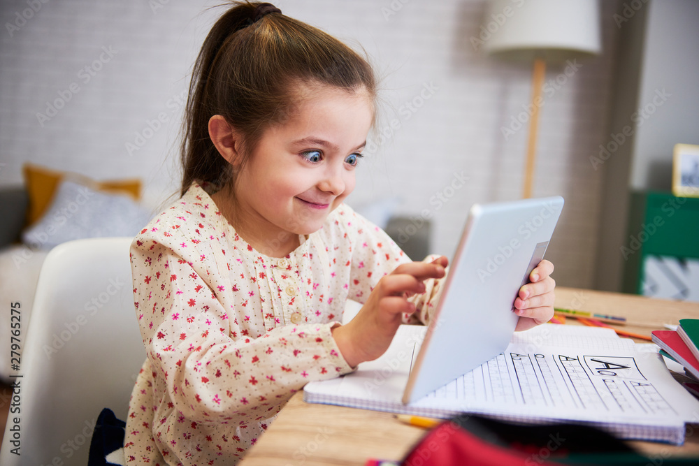 Playful child using a tablet while doing his homework at home Playful child using a tablet while doing his homework at home